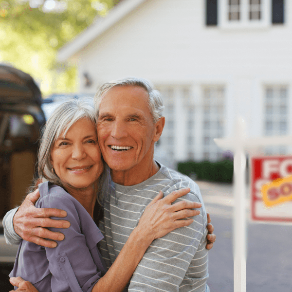 older couple with for sale sign in background